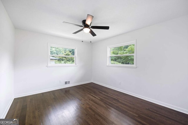 unfurnished room featuring visible vents, baseboards, dark wood-type flooring, and a healthy amount of sunlight