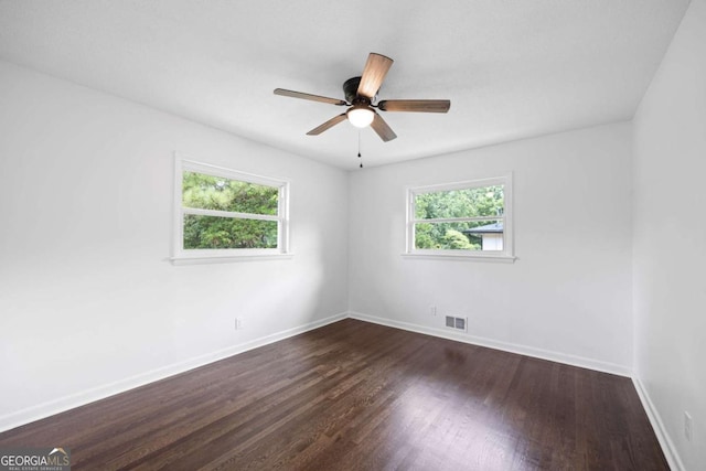 empty room featuring visible vents, dark wood-style floors, a healthy amount of sunlight, and baseboards