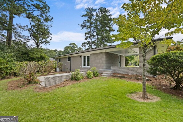 exterior space with brick siding, entry steps, french doors, and a yard