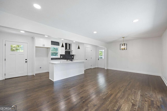 kitchen featuring tasteful backsplash, light countertops, dark wood-style flooring, and wall chimney range hood