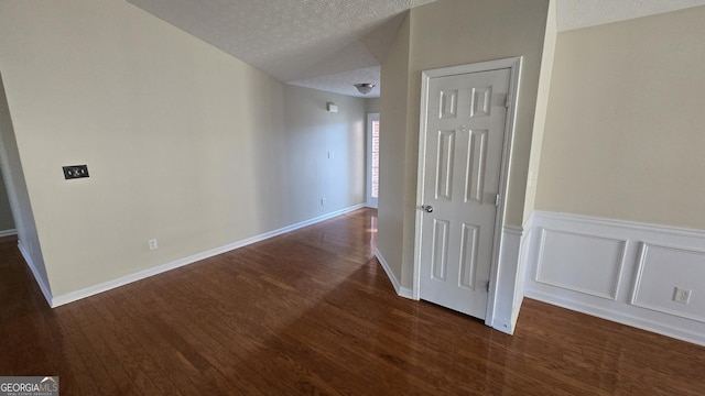 interior space with a decorative wall, dark wood-style floors, a wainscoted wall, and a textured ceiling