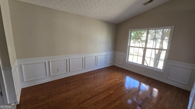 empty room featuring visible vents, dark wood-type flooring, a textured ceiling, wainscoting, and lofted ceiling