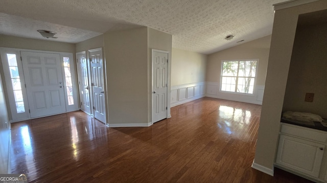 entrance foyer with dark wood finished floors, vaulted ceiling, wainscoting, a decorative wall, and a textured ceiling