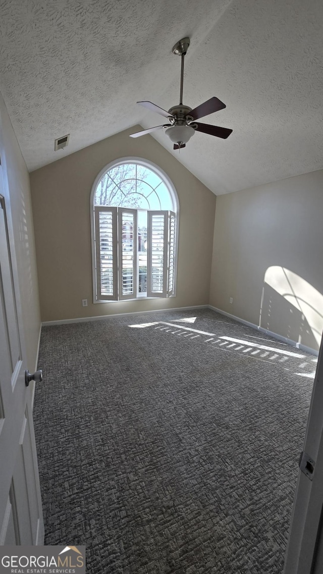 empty room featuring a ceiling fan, carpet, visible vents, lofted ceiling, and a textured ceiling