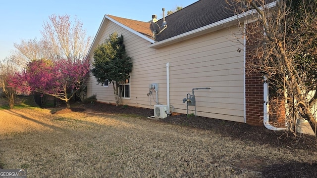 view of home's exterior featuring ac unit, a lawn, and roof with shingles