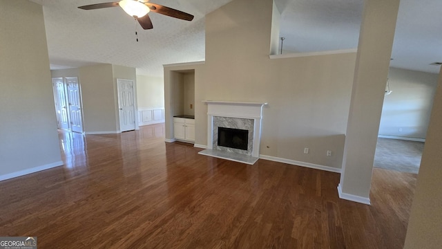 unfurnished living room featuring a high end fireplace, baseboards, ceiling fan, wood finished floors, and high vaulted ceiling