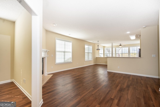 unfurnished living room featuring a tiled fireplace, dark wood finished floors, baseboards, and ceiling fan