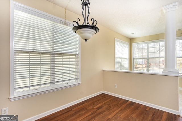 unfurnished dining area with baseboards, a textured ceiling, wood finished floors, and ornate columns