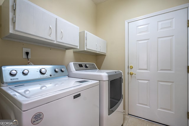 clothes washing area featuring light tile patterned floors, cabinet space, and washing machine and dryer