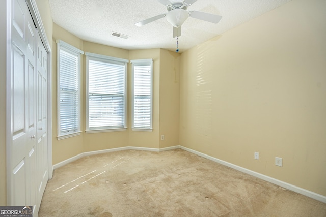 carpeted spare room featuring ceiling fan, visible vents, baseboards, and a textured ceiling