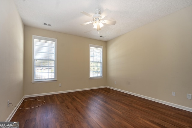 spare room featuring visible vents, dark wood-type flooring, baseboards, a textured ceiling, and a ceiling fan