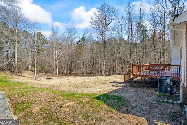 view of yard with central air condition unit, a view of trees, and a deck