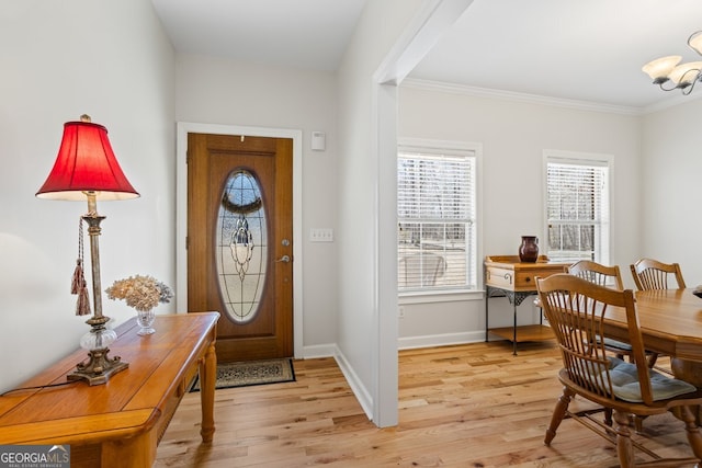 foyer entrance featuring a notable chandelier, baseboards, light wood-style floors, and crown molding