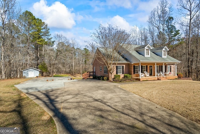 new england style home with brick siding, a front lawn, a porch, a view of trees, and an outdoor structure