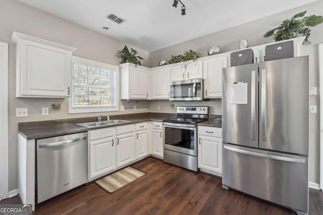2311 Fall Creek Lndg, Loganville, GA 30052 - kitchen featuring appliances with stainless steel finishes, dark countertops, dark wood finished floors, and white cabinets