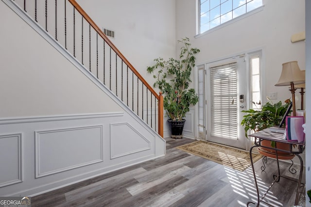 entrance foyer featuring visible vents, wood finished floors, stairway, a decorative wall, and a towering ceiling