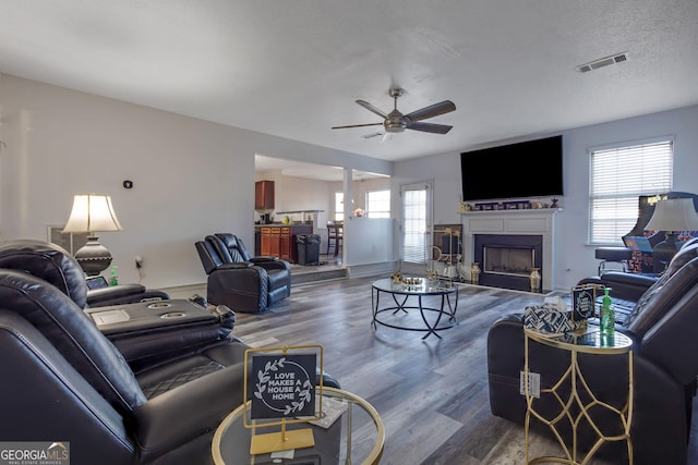 living area with wood finished floors, visible vents, a fireplace, ceiling fan, and a textured ceiling