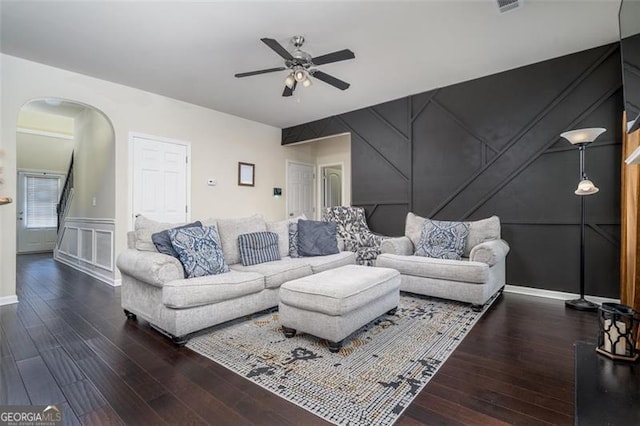 living area featuring arched walkways, wood finished floors, a ceiling fan, and a decorative wall