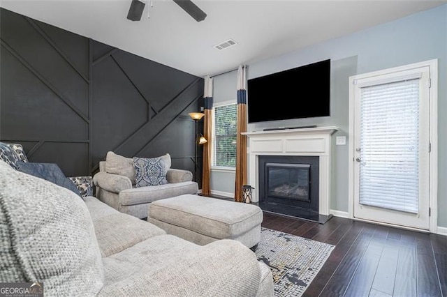 living area with baseboards, visible vents, ceiling fan, hardwood / wood-style flooring, and a glass covered fireplace