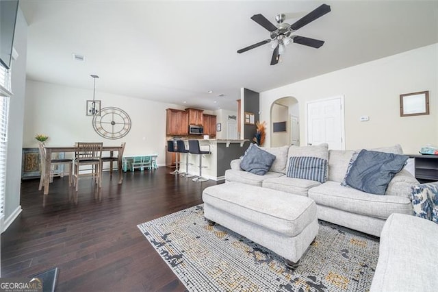 living area featuring visible vents, baseboards, ceiling fan, arched walkways, and dark wood-style flooring