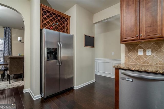 kitchen featuring tasteful backsplash, light stone countertops, dark wood finished floors, arched walkways, and stainless steel appliances