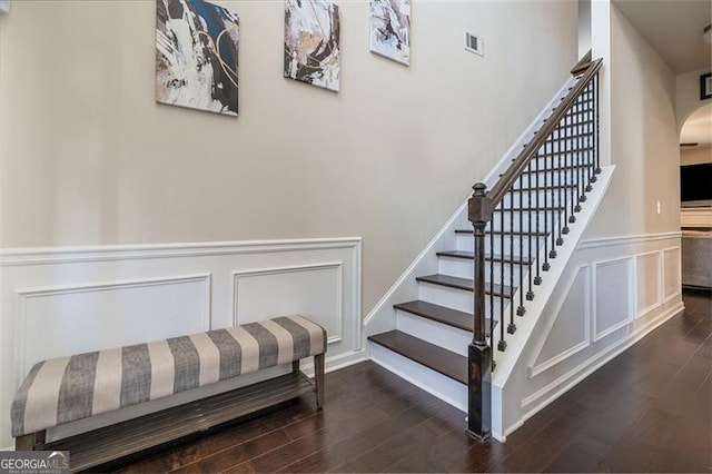 stairway with visible vents, a wainscoted wall, wood finished floors, arched walkways, and a decorative wall