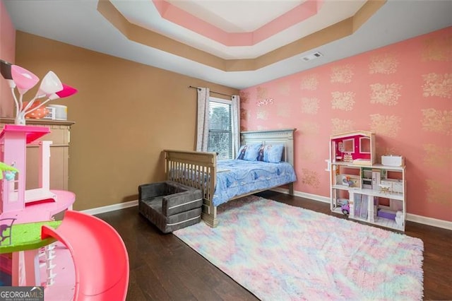 bedroom with visible vents, a raised ceiling, baseboards, and wood finished floors