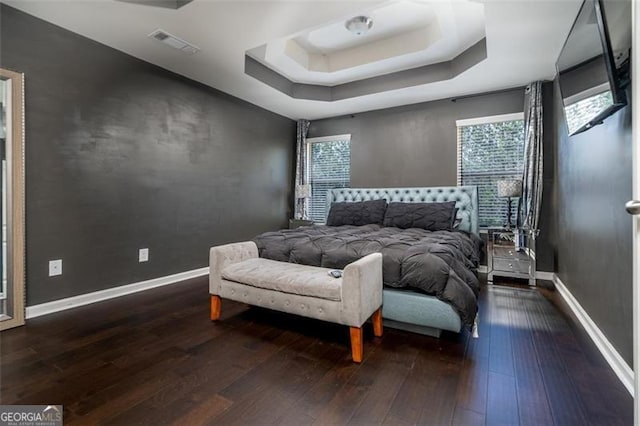 bedroom featuring dark wood finished floors, visible vents, a raised ceiling, and baseboards