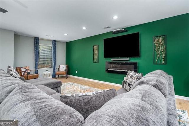 living room featuring visible vents, baseboards, wood finished floors, and an accent wall