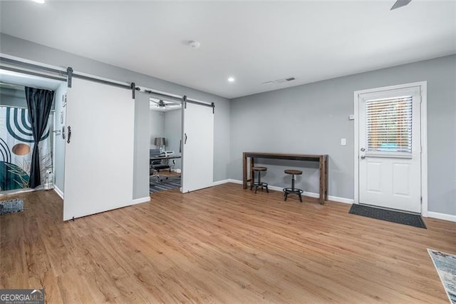 interior space with a barn door, light wood-style flooring, recessed lighting, and baseboards