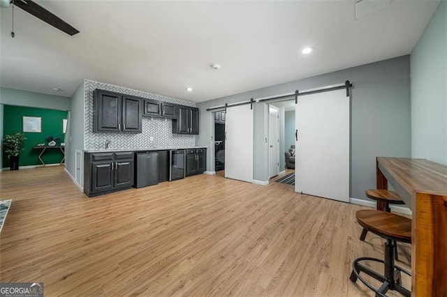 kitchen featuring a ceiling fan, light wood-style floors, stainless steel dishwasher, a barn door, and backsplash