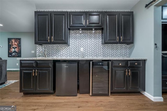 kitchen featuring baseboards, beverage cooler, a barn door, dark cabinetry, and light wood-style floors