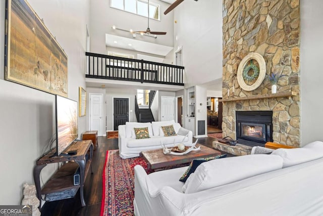 living area featuring a stone fireplace, stairs, wood finished floors, and a ceiling fan