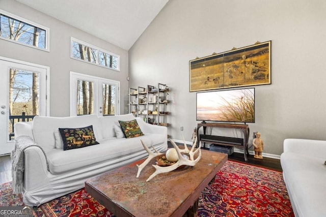 living room featuring high vaulted ceiling, baseboards, and wood finished floors