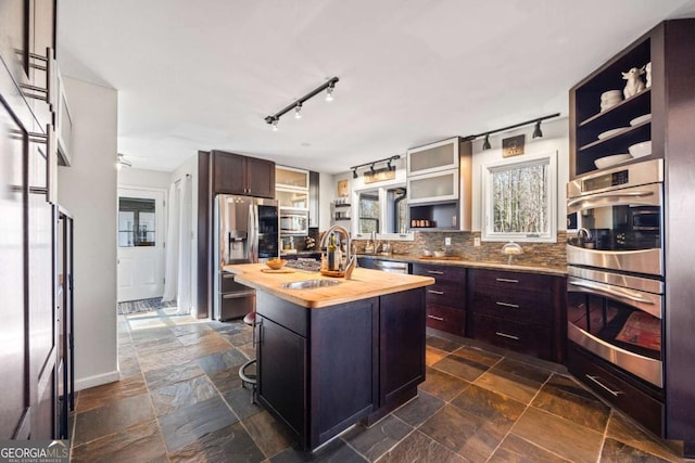 kitchen with a sink, wooden counters, stone tile floors, appliances with stainless steel finishes, and open shelves