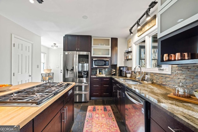 kitchen featuring light stone countertops, a sink, glass insert cabinets, appliances with stainless steel finishes, and backsplash