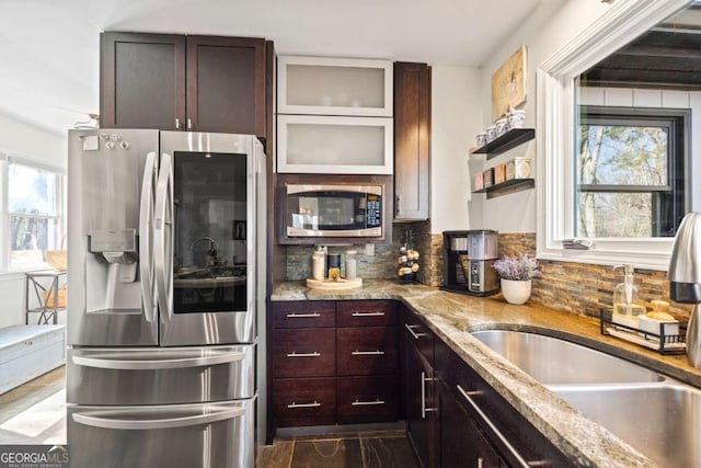 kitchen with light stone countertops, a sink, decorative backsplash, dark brown cabinetry, and appliances with stainless steel finishes