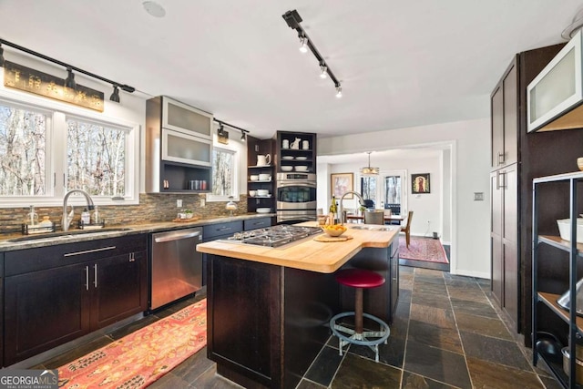 kitchen with a sink, backsplash, stone tile floors, stainless steel appliances, and wooden counters