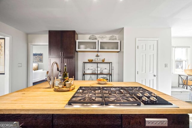 kitchen with stainless steel gas stovetop, dark brown cabinets, and glass insert cabinets