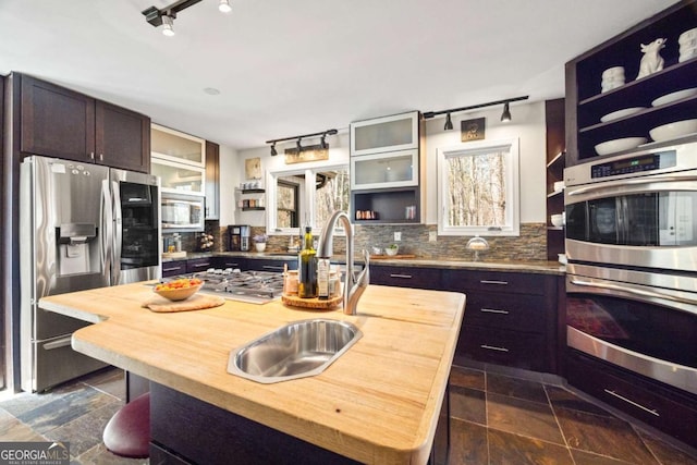 kitchen featuring open shelves, a sink, appliances with stainless steel finishes, backsplash, and butcher block counters