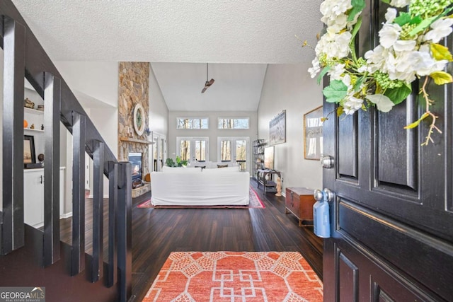 foyer entrance featuring a stone fireplace, lofted ceiling, wood finished floors, and a textured ceiling