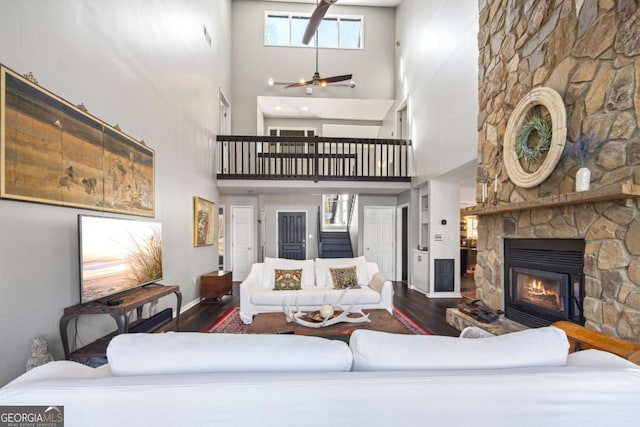 living room featuring a stone fireplace, stairs, wood finished floors, and a ceiling fan