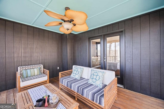 sitting room with wooden walls, french doors, light wood-type flooring, and ceiling fan