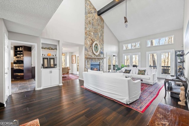 living area featuring beamed ceiling, a stone fireplace, washer / dryer, french doors, and wood finished floors