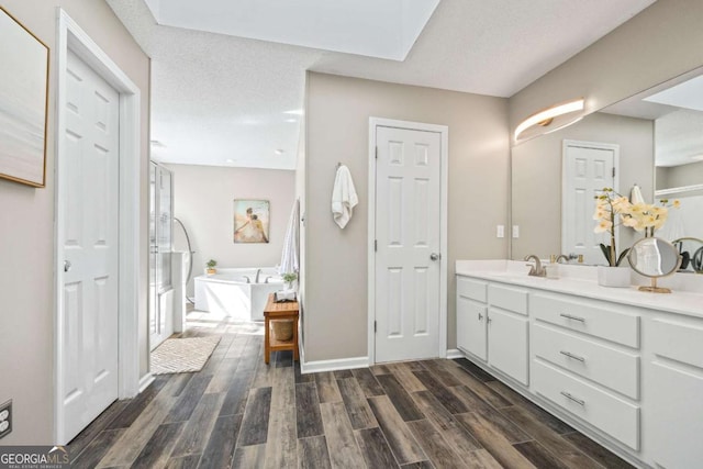 full bath featuring wood finish floors, a freestanding tub, baseboards, and vanity