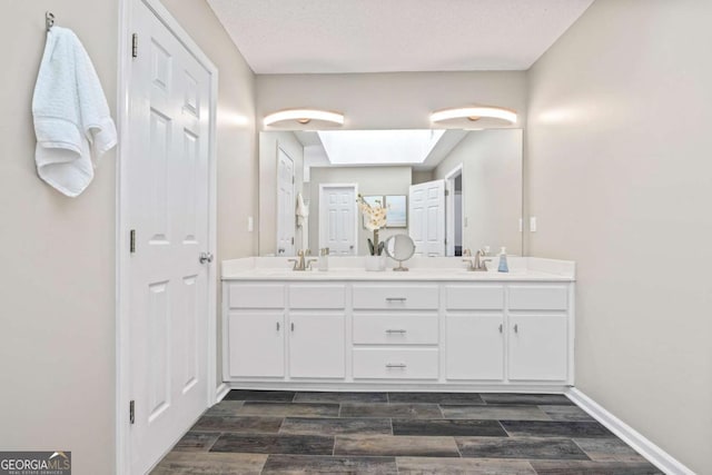 bathroom with wood finish floors, a skylight, double vanity, and a sink