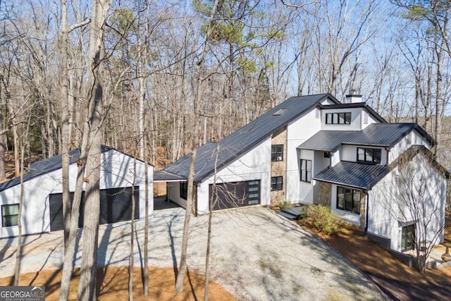 view of side of property with a chimney, metal roof, a garage, driveway, and a standing seam roof