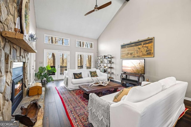 living area with high vaulted ceiling, a ceiling fan, hardwood / wood-style floors, french doors, and a stone fireplace