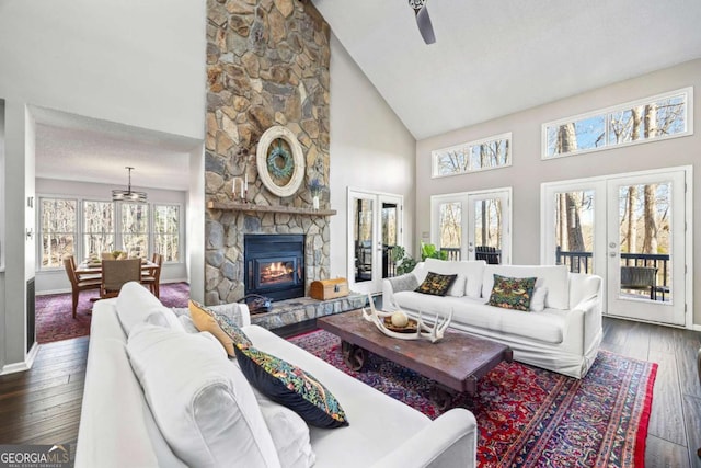 living area featuring dark wood-type flooring, high vaulted ceiling, french doors, a stone fireplace, and baseboards