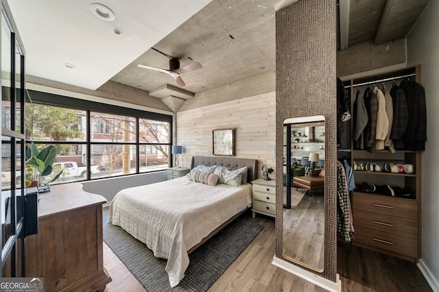 bedroom featuring a closet, wooden walls, ceiling fan, and wood finished floors